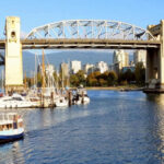 A small ferry boat sails in a harbor in front of a bridge.